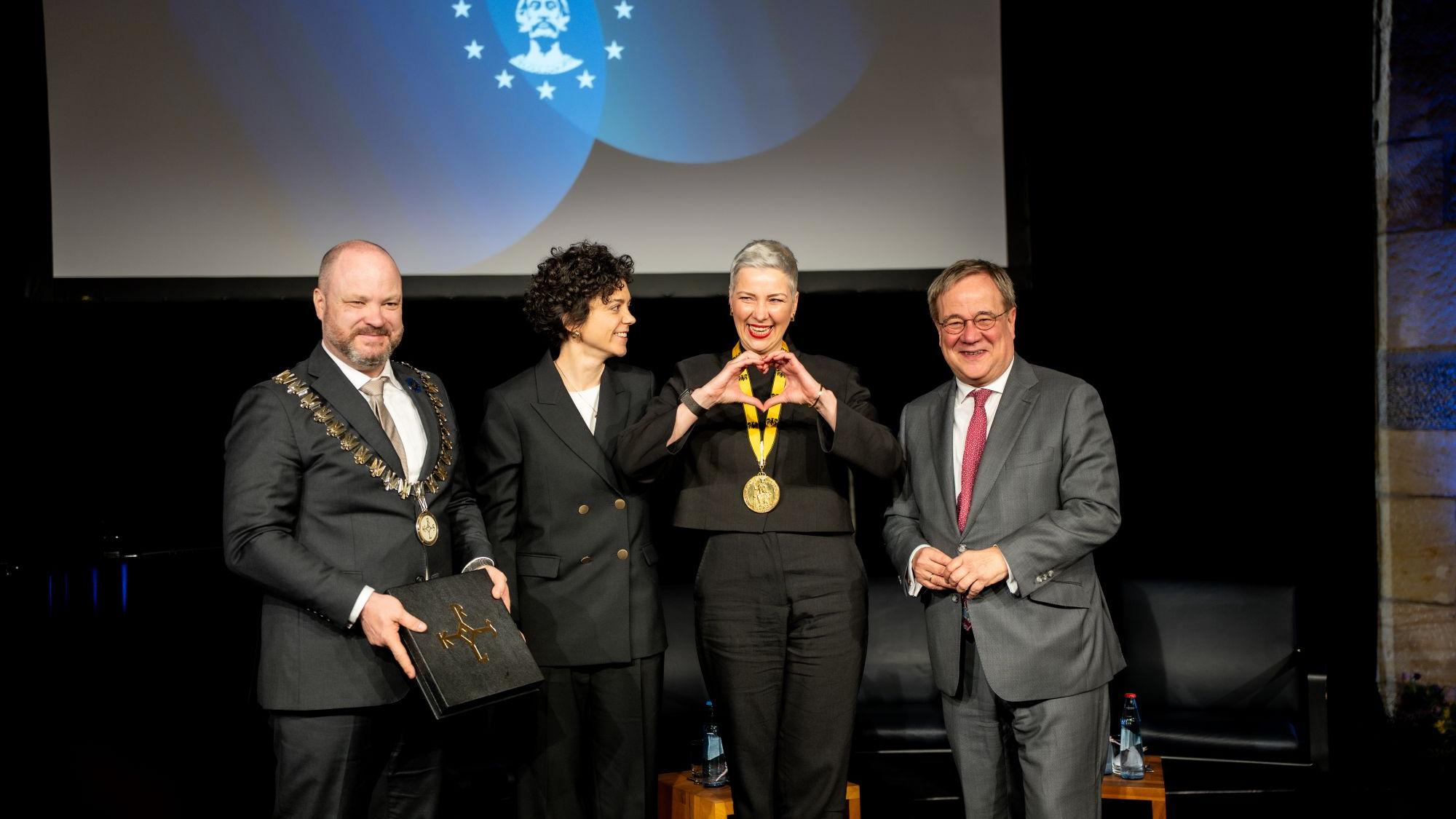 Maria Kalesnikava erhält den Karlspreis aus den Händen ihrer Schwester Tatsina Khomich. Michael Ziemons, Oberbürgermeister der Stadt Aachen, und Armin Laschet, Vorsitzender des Karlspreis-Direktoriums, sind die ersten Gratulanten.