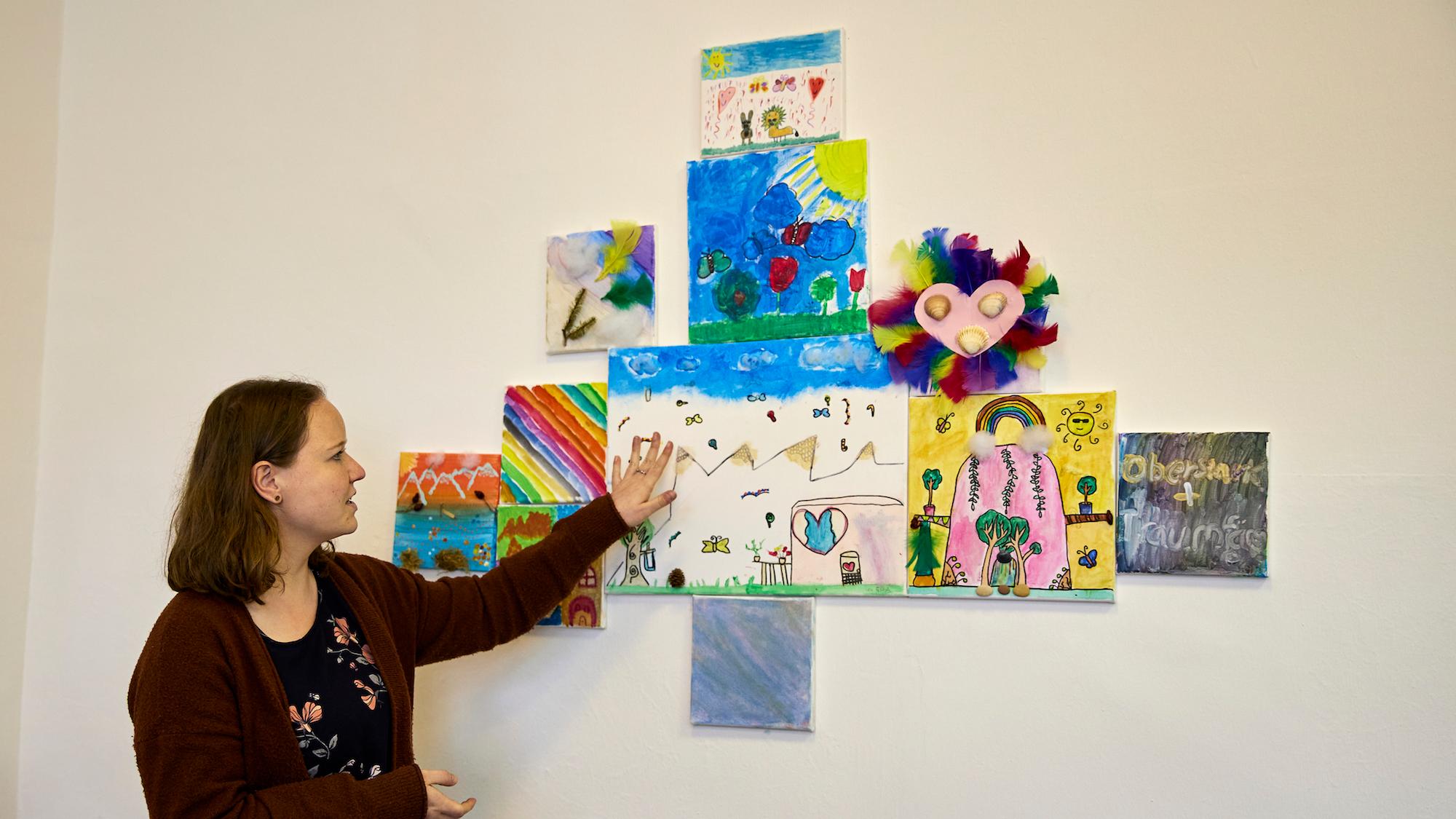 Ellen Sachsenmaier zeigt die Ergebnisse eines kunsttherapeutischen Angebots, bei dem die Kinder einen sicheren Ort malen sollten. An diesen Ort können sie sich gedanklich zurückziehen, wenn sie Stress oder Angst haben. (c) Caroline Schaefer/Caritas international