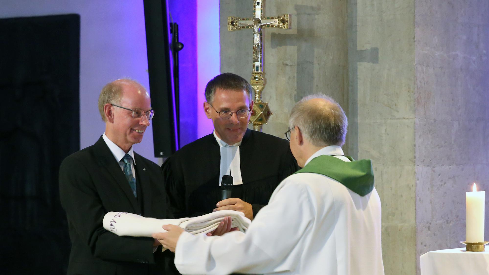 Propst Peter Blättler übergibt das Mönchengladbacher Altartuch an die evangelischen Geschwister Pfarrer Stephan Dedring (l.) und Pfarrer Till Hüttenberger. (c) Detlef Ilgner