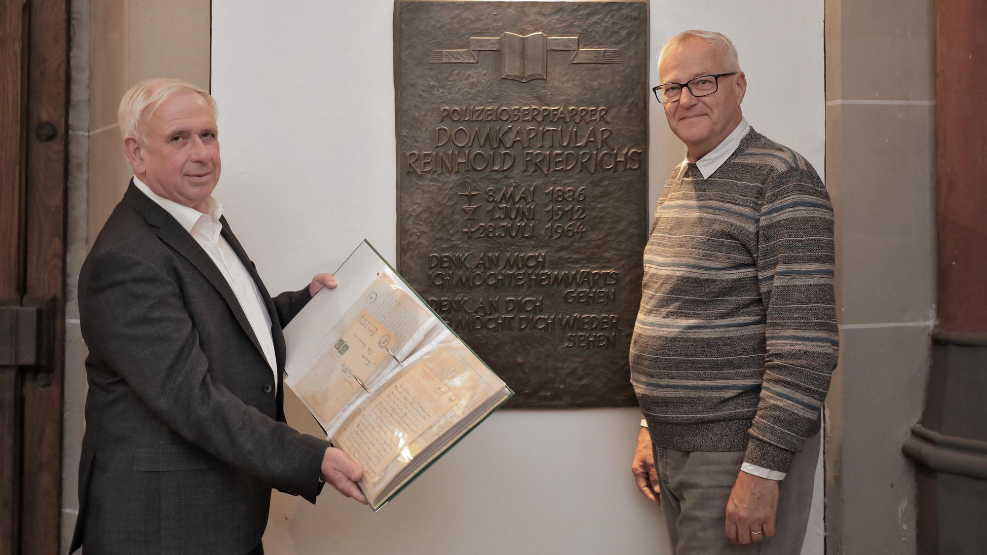 Pfarrer Paul Jansen (l., mit den Originalbriefen) und Gregor  Micus vor der Grabplatte von Domkapitular Reinhold Friedrichs. (c) Dirk Jochmann