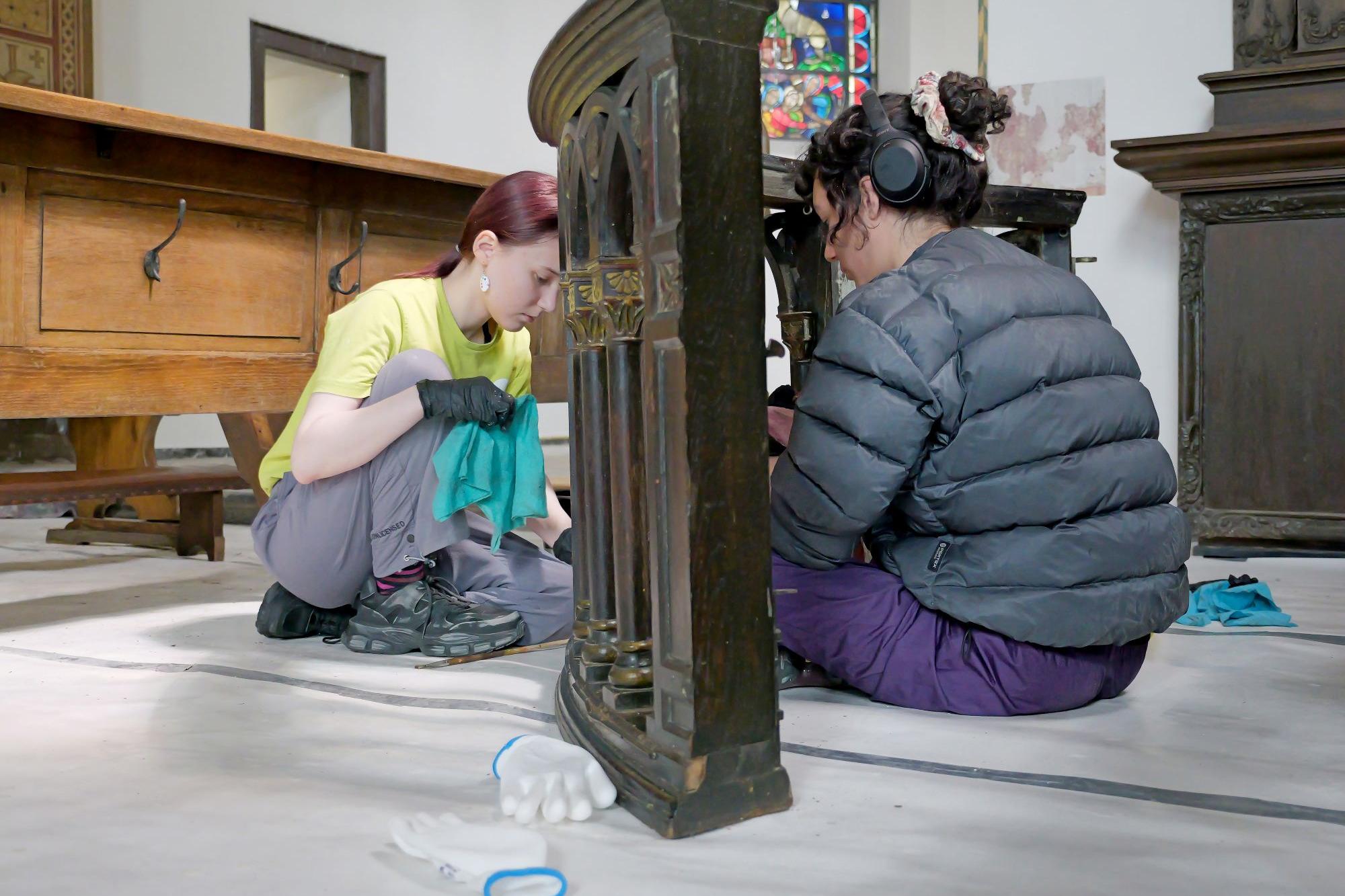 Mit Feingefühl: Elianne (li.) und Elena entfernen den Schlamm von einer alten Kirchenbank.