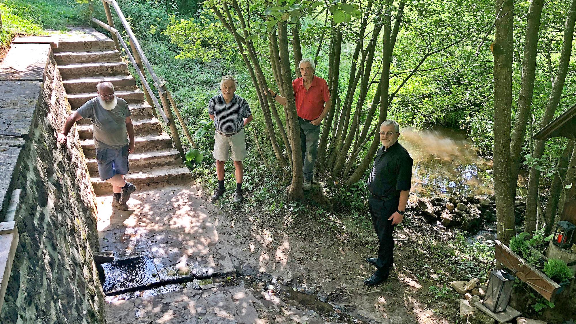 Georg Zander aus Sistig, Heinz Hermanns aus Broich, sein  Namenszwilling Heinz Hermanns aus Sistig und der Steinfelder Pater Wieslaw Kaczor SDS am aufgeräumten und freigeschnittenen Platz im Kuttenbachtal. (c) Gudrun Klinkhammer